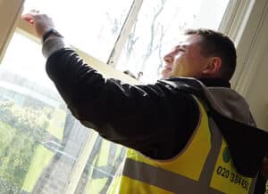 Man in a high-visibility vest inspecting sash window restoration, showcasing professional property maintenance and brick cleaning services.
