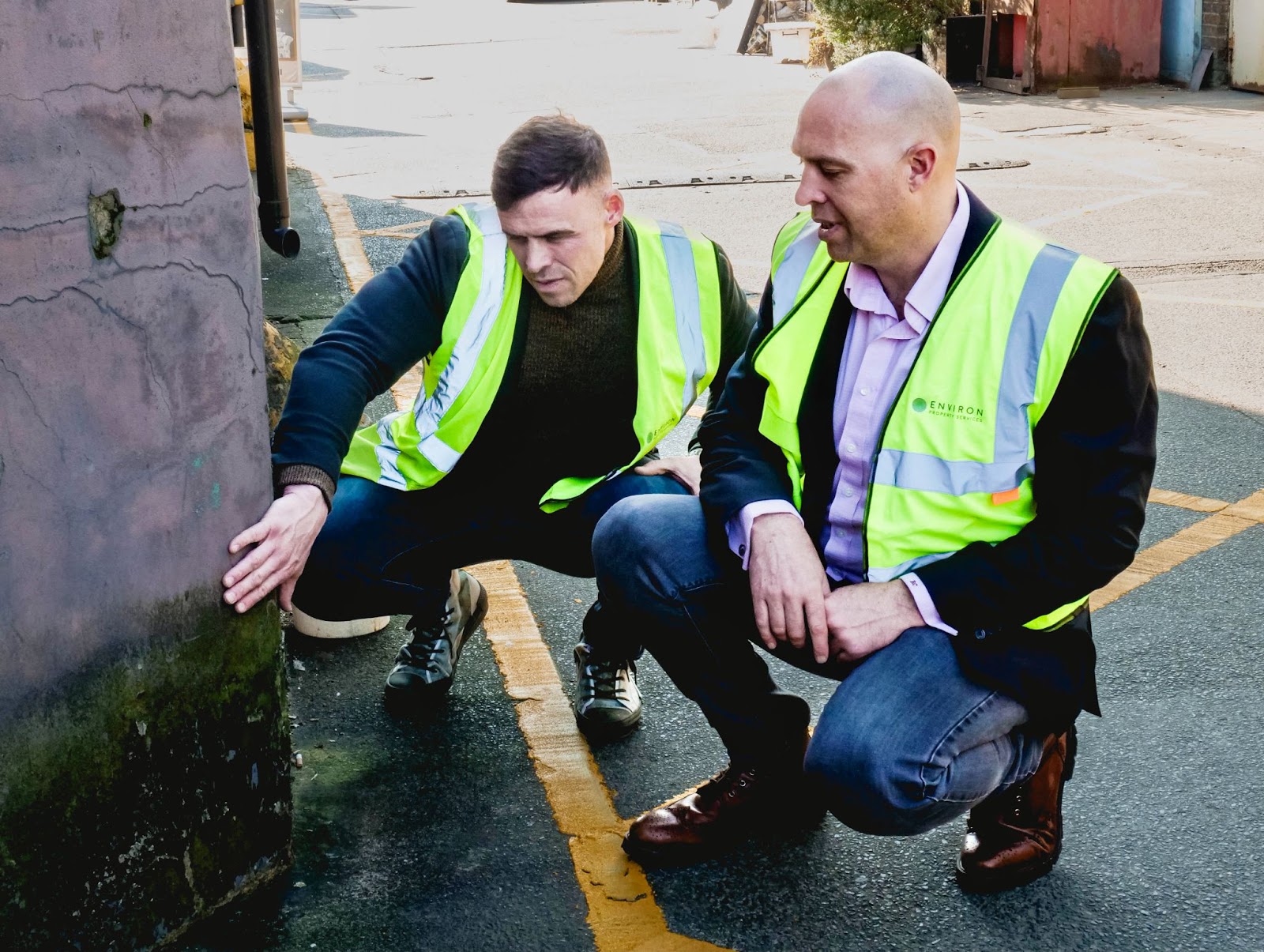 Two professionals in high-visibility jackets inspecting damp on a wall, emphasizing moisture assessment and restoration services.