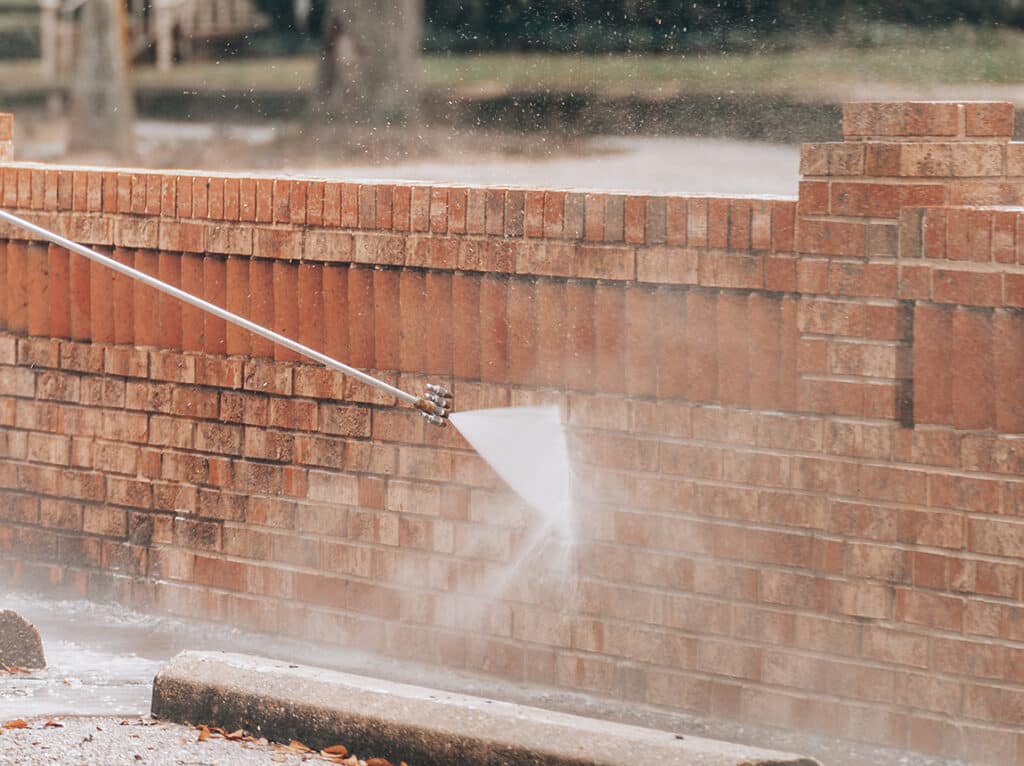 Person using a pressure washer to clean a brick wall, showcasing maintenance techniques for brickwork restoration.