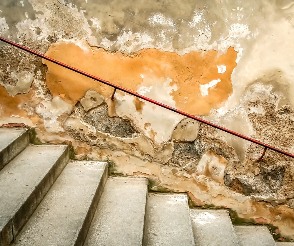 Staircase with concrete steps and a wall showing signs of penetrating damp, including peeling paint and discolouration, highlighting moisture damage issues relevant to damp proofing services.