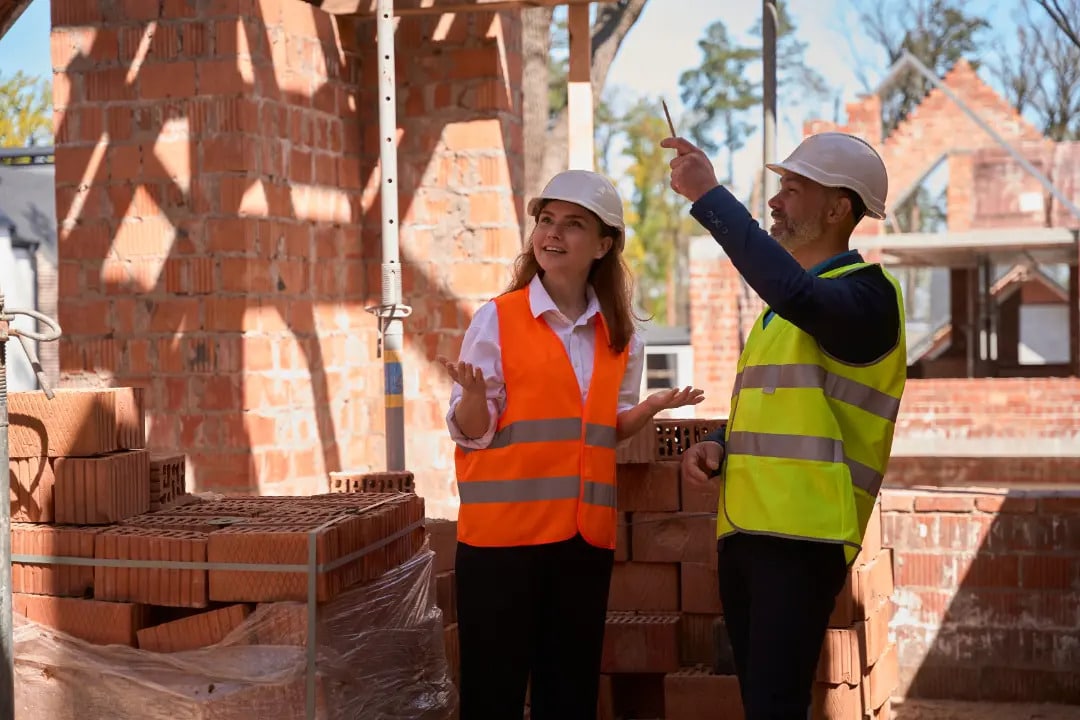 Construction professionals discussing brickwork assessment on a building site, surrounded by stacks of bricks, emphasizing the importance of structural integrity in preventing damp issues.