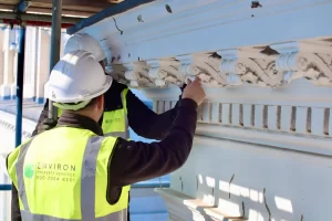 Workers in hard hats and high-visibility vests restoring ornate cornice details on a heritage building, highlighting Environ Restoration Services' expertise in architectural preservation.