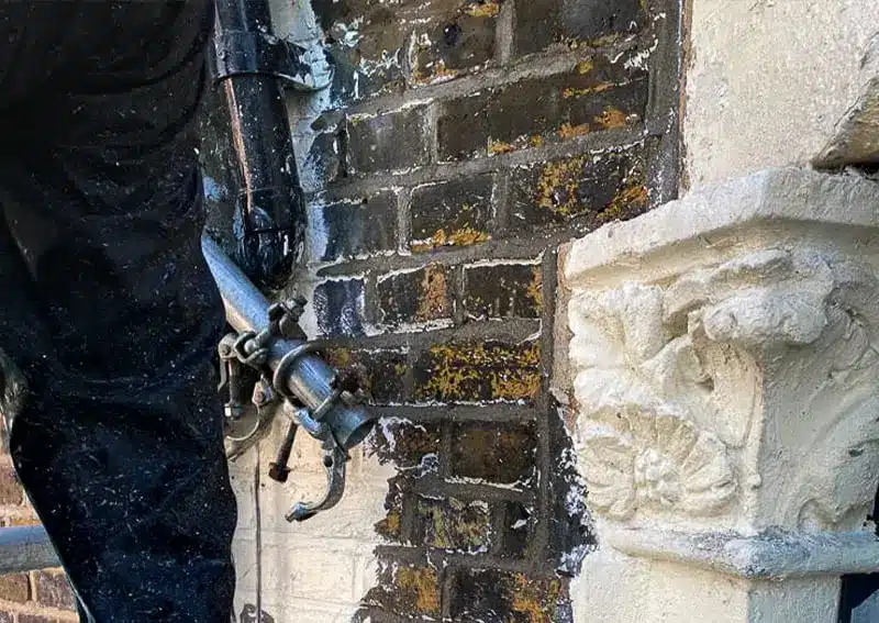 Worker using ThermaTech technology for brick paint removal, revealing natural brick surface and ornate stonework detail.
