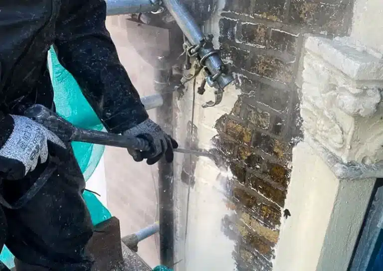 Worker using a pneumatic tool to restore brickwork on a historic building, showcasing period property conservation techniques in London.
