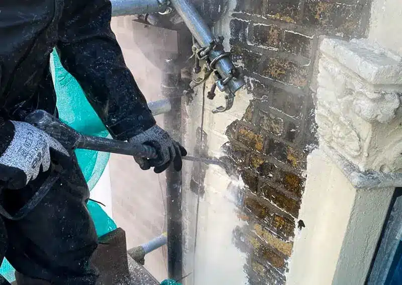 Worker using high-pressure equipment to remove paint from brick wall, showcasing brick restoration process in London.