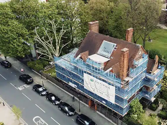 Scaffolded communal property undergoing restoration in London, surrounded by trees and parked cars, highlighting Section 20 works.