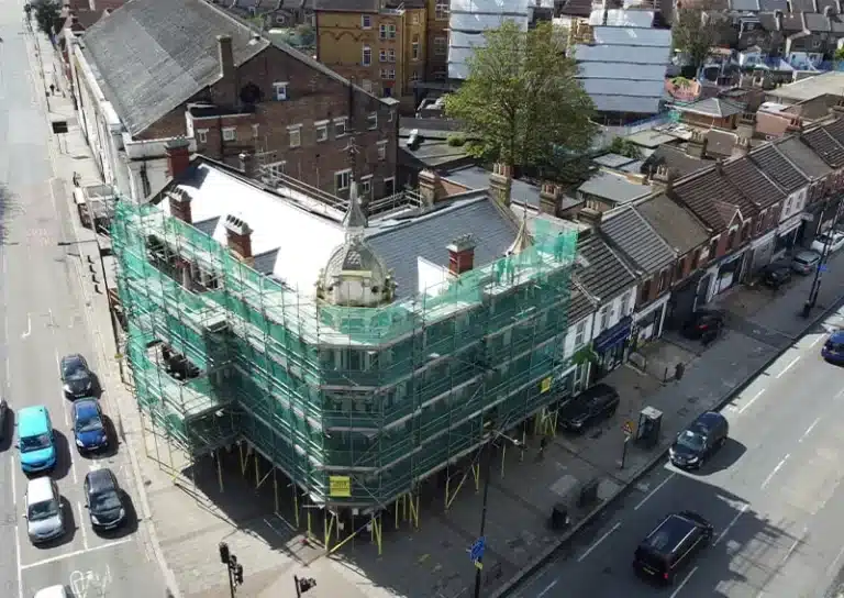 Building under renovation with scaffolding and green mesh, showcasing facade cleaning and restoration services by Environ Restoration Services in London.