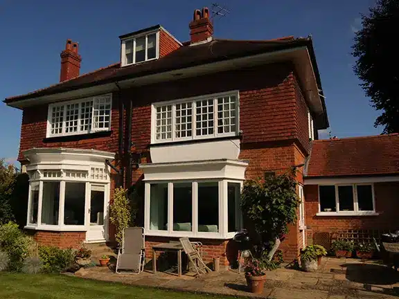 Traditional brick house with multiple windows, surrounded by greenery and garden elements, showcasing potential for stone wall restoration services by Environ Restoration.