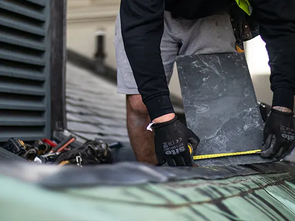 Worker installing slate roofing on a period building, showcasing craftsmanship and attention to detail in restoration services.