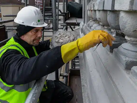 Restoration expert in safety gear working on listed building details, showcasing traditional craftsmanship and attention to historical integrity.
