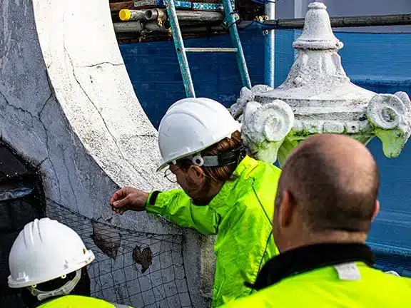 Team of restoration experts inspecting a listed building, wearing safety helmets and high-visibility jackets, examining architectural details, scaffolding in the background, highlighting the restoration process.