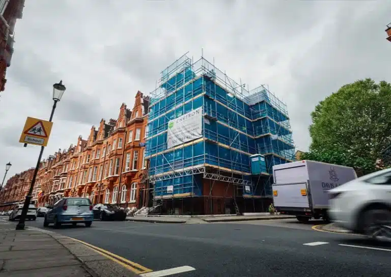Victorian house under restoration, covered in scaffolding and blue protective sheeting, featuring Environ Restoration Services branding, surrounded by classic architecture and vehicles on the street.