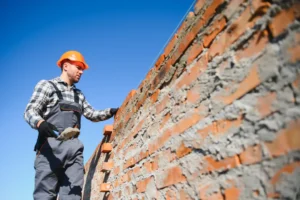 Construction worker in helmet applying mortar to brick wall, highlighting professional repointing techniques for property restoration.