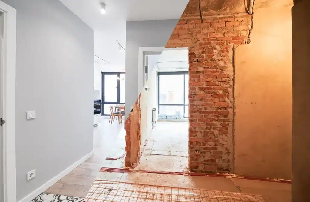 Interior renovation showcasing a divided space with exposed brick wall on one side and modern, grey-painted wall on the other, illustrating the contrast between restoration and renovation.
