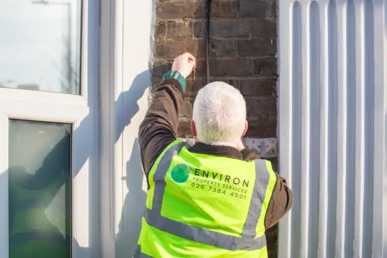 Worker in high-visibility vest inspecting a building, showcasing Environ Restoration Services branding, emphasizing property assessments and restoration expertise.