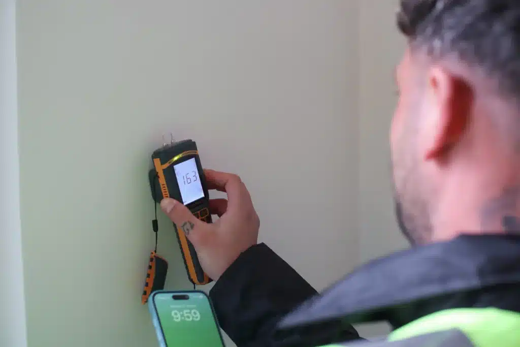 Person using a damp meter to assess moisture levels in a wall, emphasizing the importance of moisture management in brick cleaning and restoration.