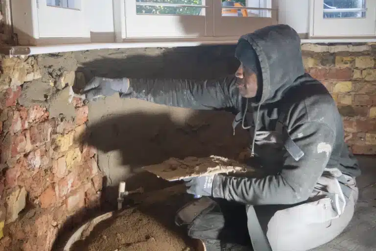 Professional worker applying damp-proofing treatment to brick wall in London home, highlighting restoration efforts against damp issues.