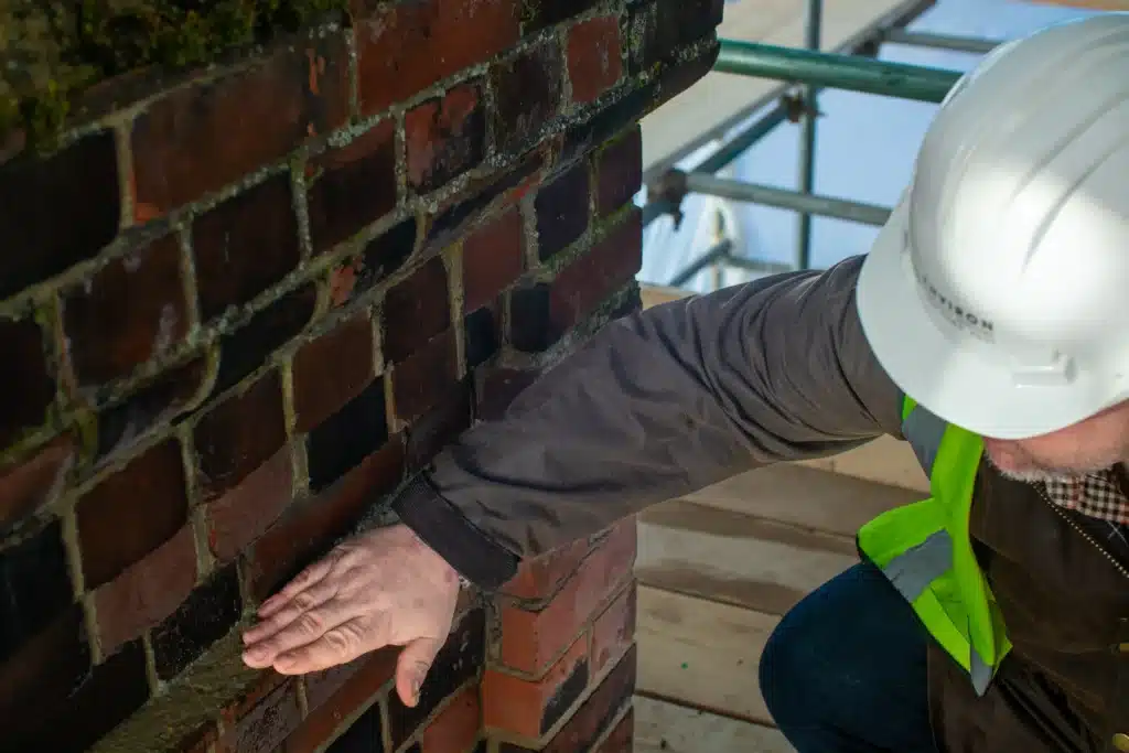 Construction professional assessing brick wall condition, highlighting restoration techniques for historic properties, with scaffolding in background.