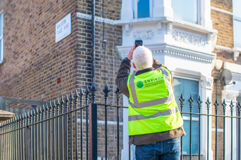 Surveyor in high-visibility jacket taking photo of historic building façade for restoration assessment.