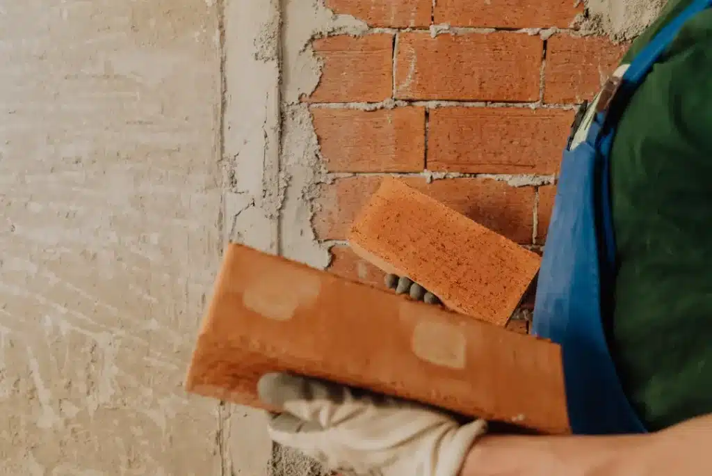 Person in blue overalls holding a brick, preparing for masonry work on a brick wall, illustrating professional brick cleaning and restoration services.