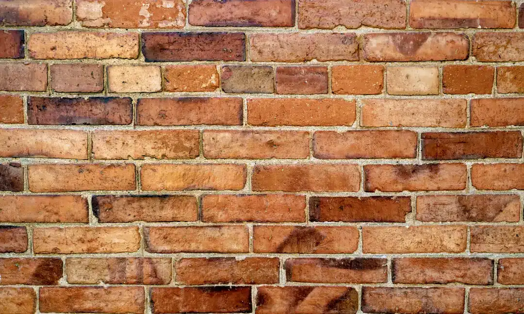 Brick wall with varied tones and textures, illustrating the importance of masonry inspections and repointing for structural integrity and aesthetic appeal in building restoration.