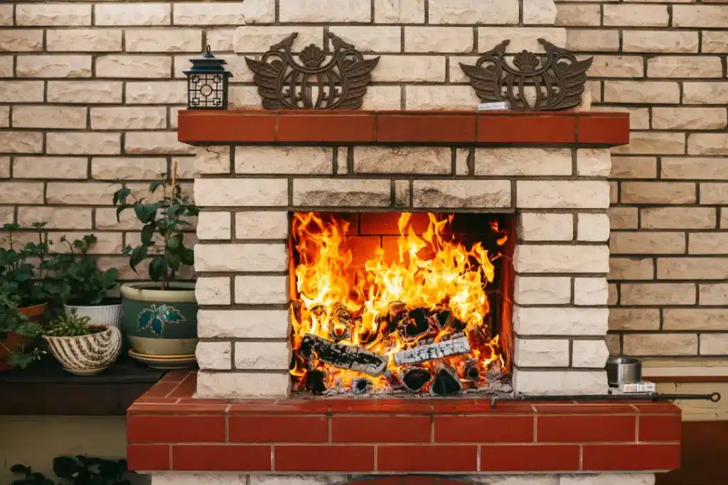 Fireplace with roaring flames and clean brickwork, surrounded by potted plants, highlighting the importance of maintaining a welcoming and safe home ambience.