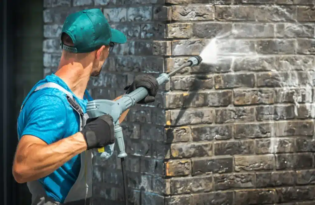 Man using a power washer to clean brick wall, demonstrating effective brick cleaning techniques for maintenance and prevention of damp and mould growth.