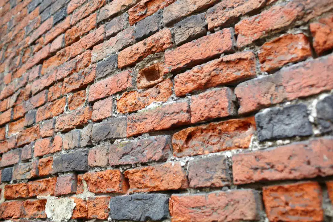 Close-up of a textured brick wall showing various shades of red and black bricks, illustrating potential underlying issues relevant to pebbledash removal and brickwork restoration.