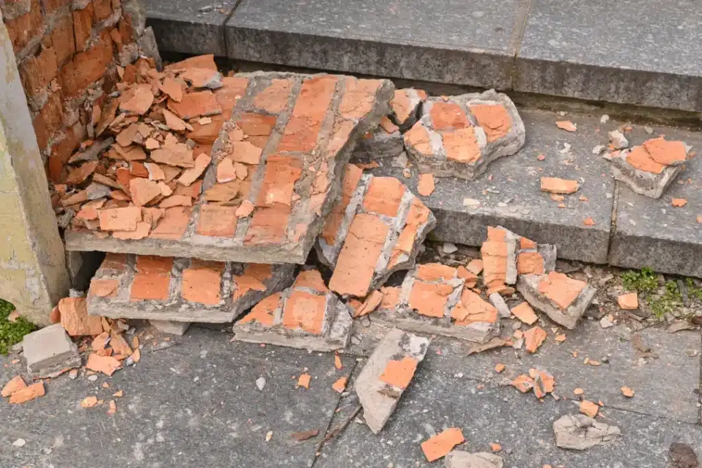 Damaged brickwork with loose bricks and debris on steps, highlighting the need for assessment before pebbledash removal.