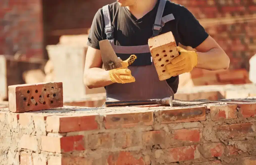 Construction worker inspecting bricks with trowel and gloves, focusing on quality assessment for brick restoration and cleaning.
