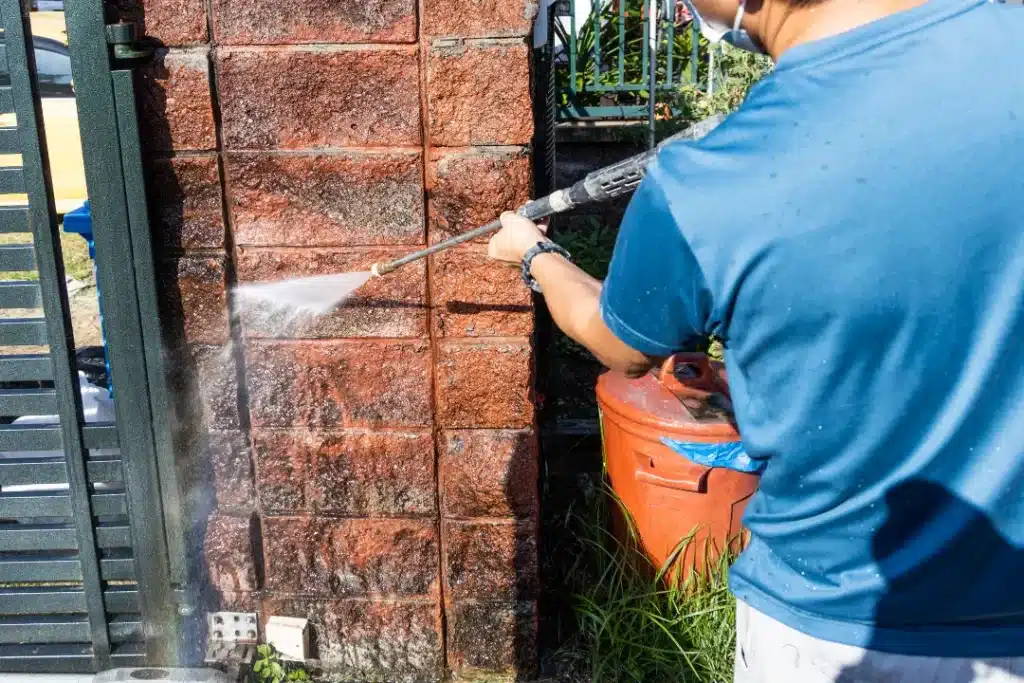 Person using a pressure washer to clean a brick wall, demonstrating effective cleaning methods for brick surfaces.