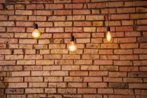 Three pendant lights illuminating a textured brick wall, highlighting the potential for professional brick restoration and maintenance.