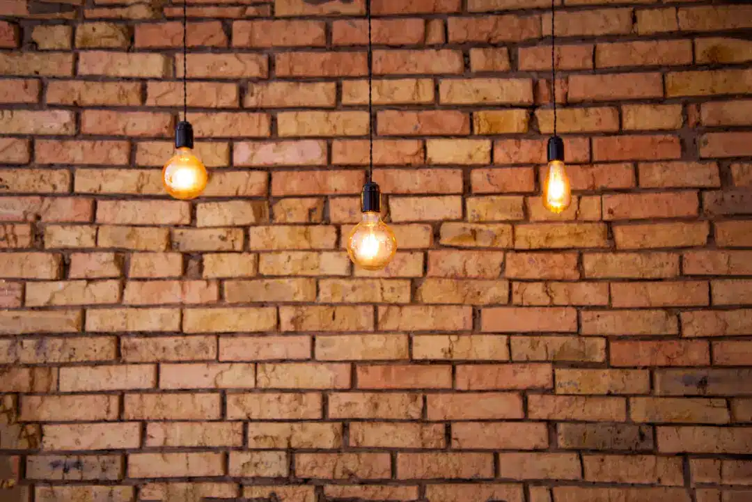 Hanging vintage light bulbs illuminating a textured brick wall, highlighting the potential for professional brick brightening and restoration services.