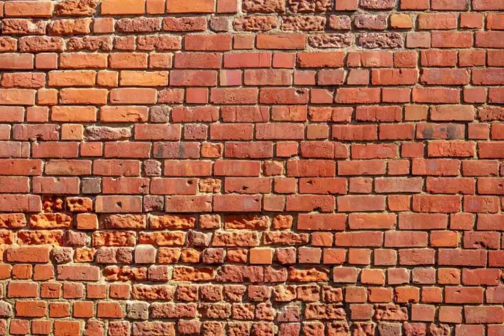 Brick wall with varying shades of red and orange, showing signs of wear and fading, illustrating the effects of grime and weathering on masonry surfaces.