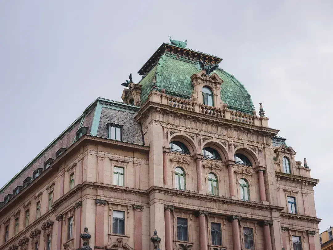 Historic building with ornate architecture, featuring a green domed roof, intricate stonework, and large arched windows, exemplifying principles of historic building conservation.